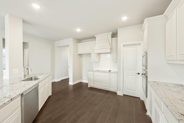 kitchen with appliances with stainless steel finishes, sink, premium range hood, white cabinetry, and light stone counters