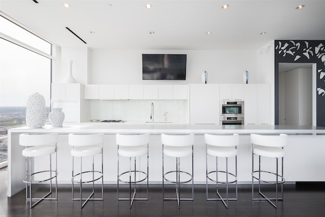 kitchen with double oven, white cabinetry, a breakfast bar area, and plenty of natural light