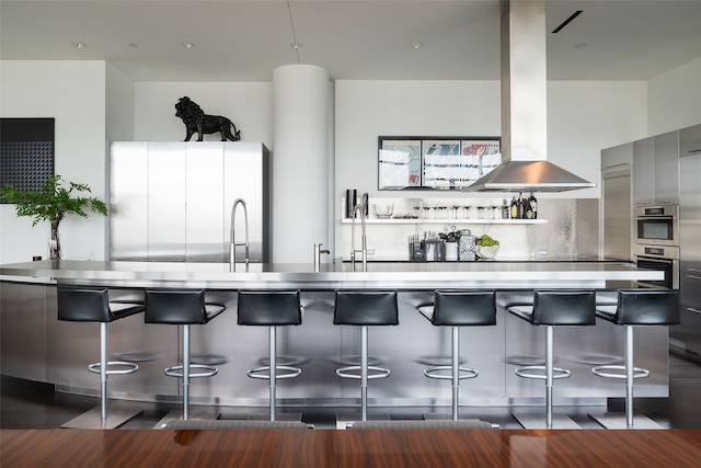 kitchen with wood-type flooring, sink, island range hood, stainless steel refrigerator, and backsplash