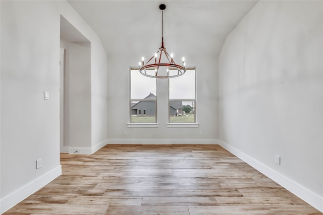 unfurnished dining area with light hardwood / wood-style floors, vaulted ceiling, and an inviting chandelier