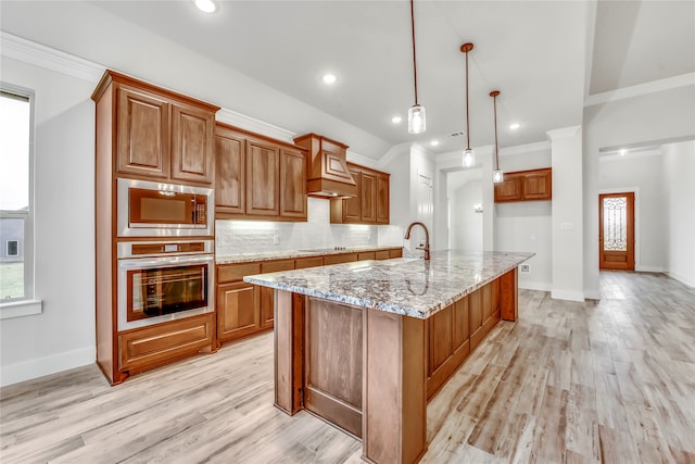 kitchen with a kitchen island with sink, light stone countertops, decorative light fixtures, light hardwood / wood-style floors, and stainless steel appliances