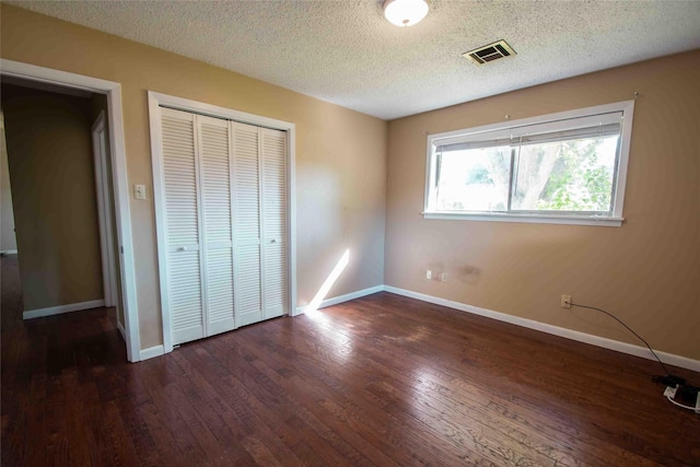 unfurnished bedroom featuring a textured ceiling, a closet, and dark hardwood / wood-style flooring