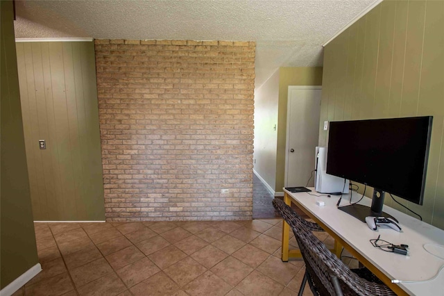 home office with light tile patterned floors, plenty of natural light, a textured ceiling, and brick wall