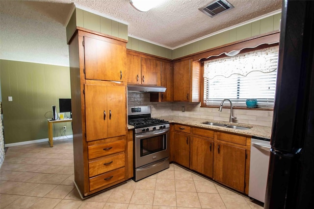 kitchen with stainless steel gas stove, sink, backsplash, light tile patterned floors, and light stone countertops