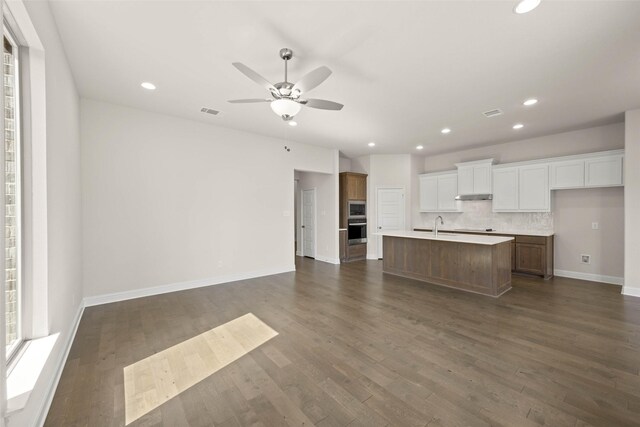 kitchen with dark wood-style flooring, open floor plan, appliances with stainless steel finishes, and a center island with sink