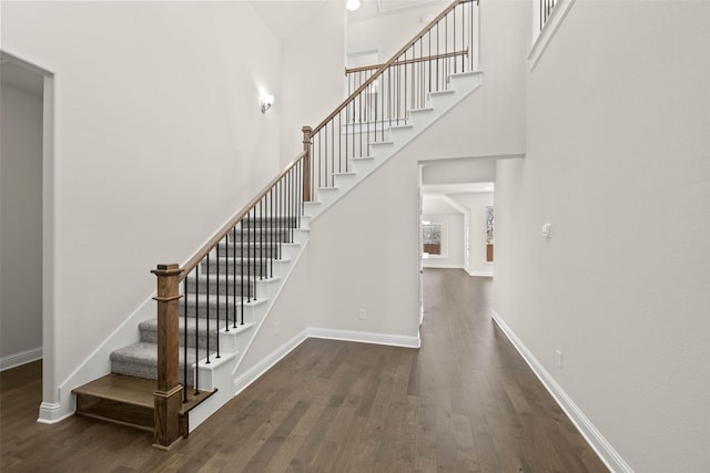 stairs with a high ceiling, wood finished floors, and baseboards