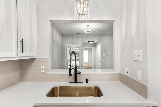 kitchen with white cabinetry, light stone countertops, sink, and an inviting chandelier