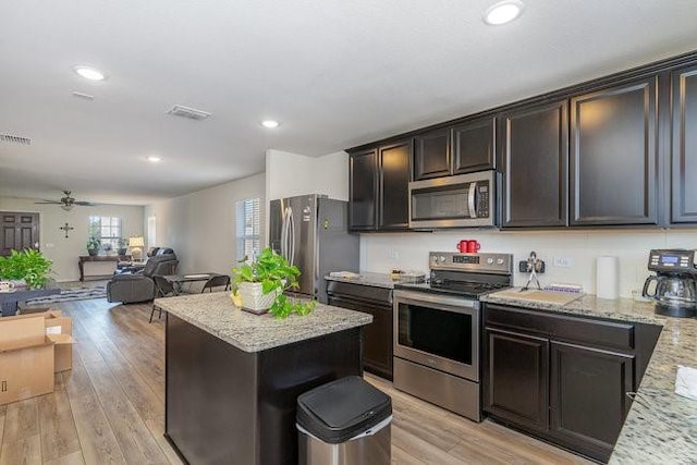 kitchen with ceiling fan, light wood-type flooring, a kitchen island, light stone counters, and stainless steel appliances