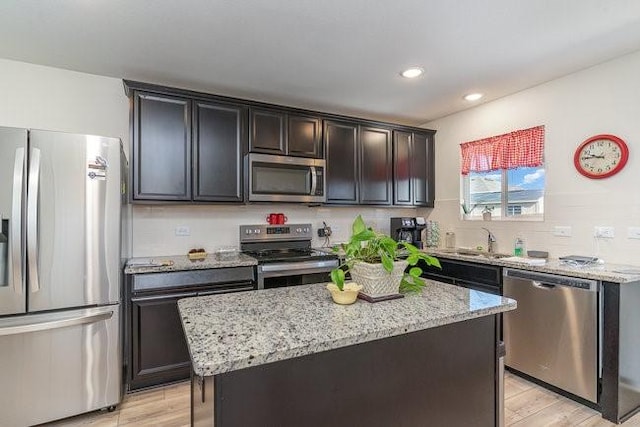 kitchen featuring sink, light hardwood / wood-style flooring, a kitchen island, light stone counters, and stainless steel appliances