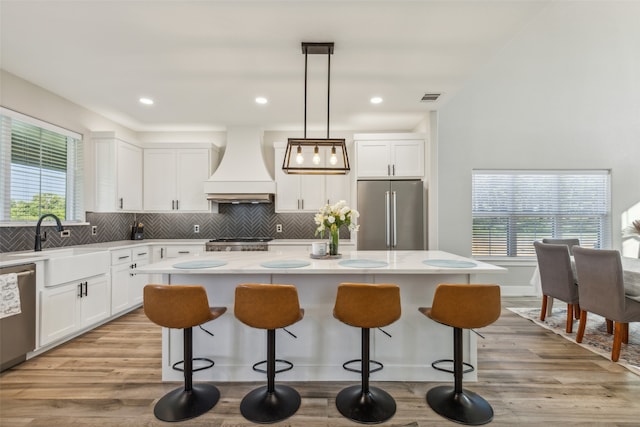 kitchen with appliances with stainless steel finishes, hanging light fixtures, light wood-type flooring, a center island, and premium range hood