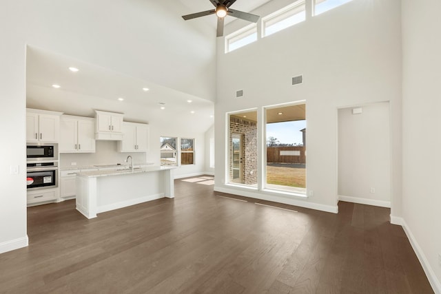 kitchen featuring a towering ceiling, oven, built in microwave, white cabinets, and an island with sink