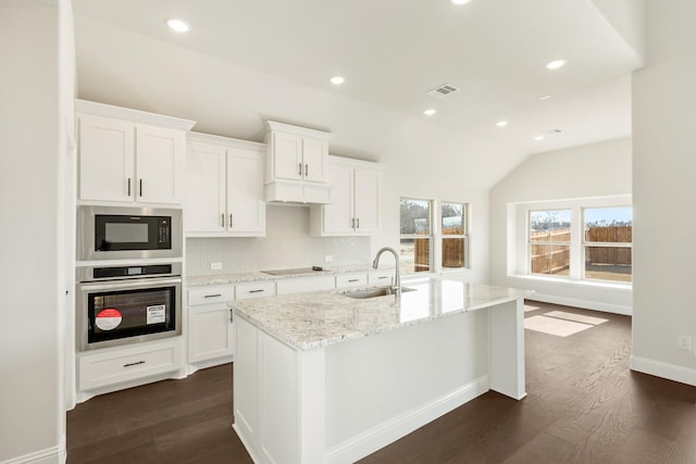 kitchen with vaulted ceiling, sink, white cabinetry, oven, and a center island with sink