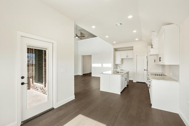 kitchen with light stone countertops, a kitchen island with sink, white cabinets, dark hardwood / wood-style flooring, and ceiling fan