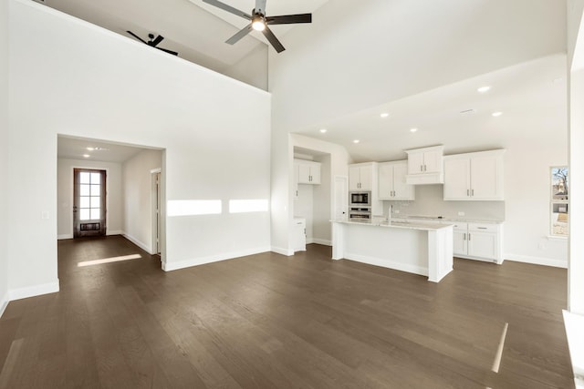 unfurnished living room featuring high vaulted ceiling, sink, dark hardwood / wood-style flooring, and ceiling fan