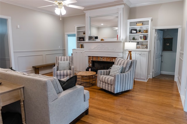 living room featuring ornamental molding, ceiling fan, a high end fireplace, and light wood-type flooring