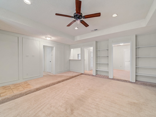 unfurnished living room with carpet flooring, a tray ceiling, ceiling fan, and a textured ceiling