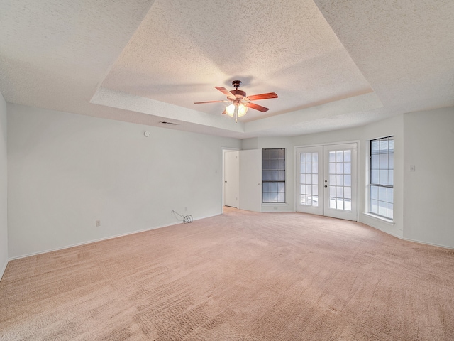 empty room featuring french doors, light colored carpet, a tray ceiling, ceiling fan, and a textured ceiling