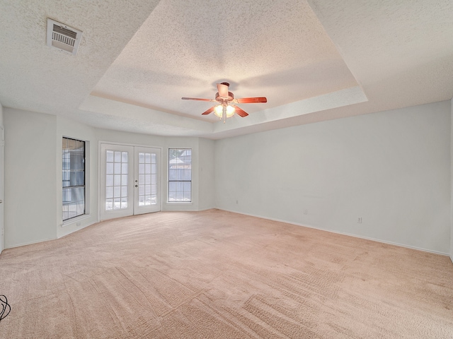 carpeted empty room featuring a raised ceiling, a textured ceiling, french doors, and ceiling fan