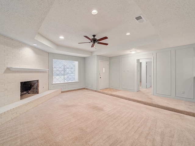 unfurnished living room with a fireplace, light carpet, a textured ceiling, ceiling fan, and a tray ceiling