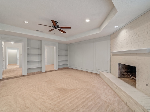 unfurnished living room featuring a fireplace, light carpet, a textured ceiling, ceiling fan, and a raised ceiling