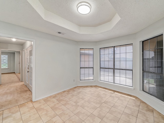 unfurnished room featuring a tray ceiling, a textured ceiling, and light tile patterned floors