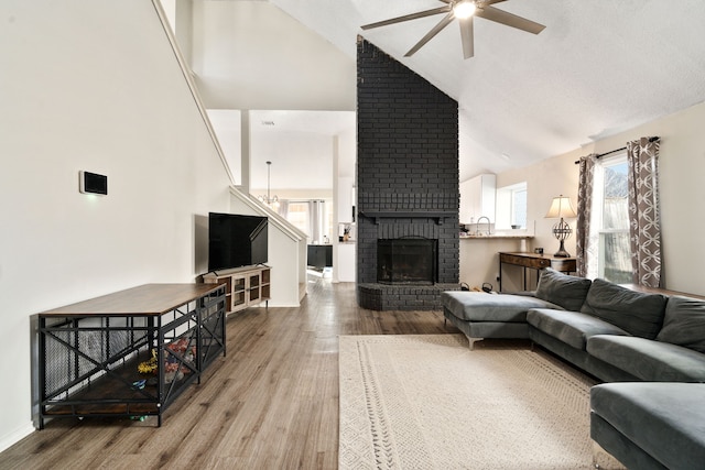 living room featuring ceiling fan, hardwood / wood-style floors, high vaulted ceiling, and a brick fireplace