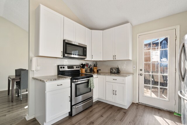 kitchen with white cabinets, appliances with stainless steel finishes, backsplash, and light stone counters