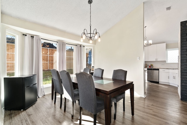 dining room with wood-type flooring, vaulted ceiling, a textured ceiling, and an inviting chandelier