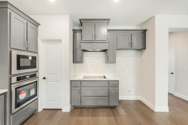 kitchen with gray cabinets, black electric stovetop, stainless steel oven, backsplash, and built in microwave