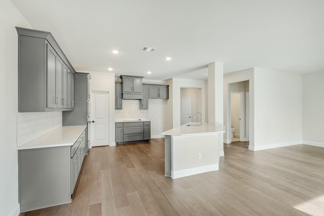 kitchen with tasteful backsplash, light hardwood / wood-style floors, sink, a kitchen island with sink, and gray cabinetry