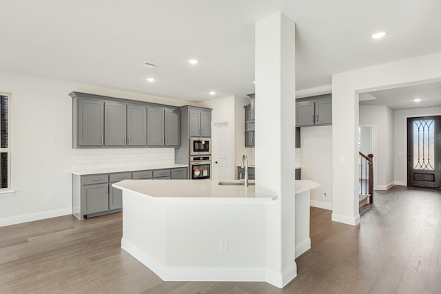 kitchen featuring decorative backsplash, sink, oven, gray cabinetry, and built in microwave