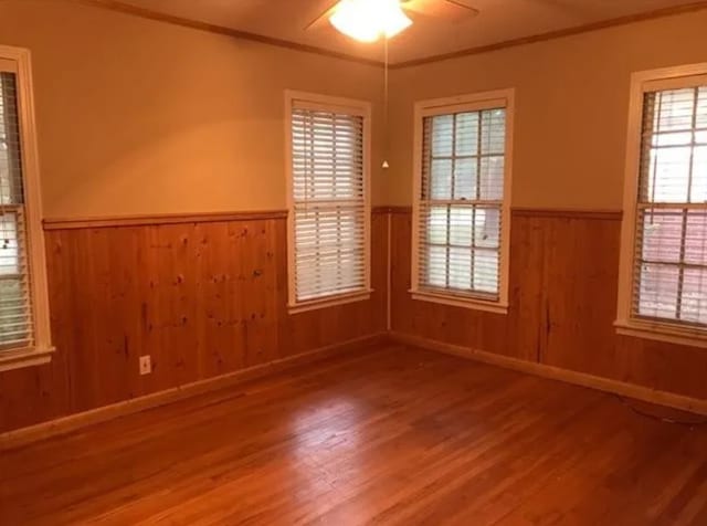 empty room with wood walls, ceiling fan, crown molding, and wood-type flooring