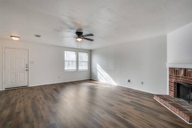 unfurnished living room with ceiling fan, dark hardwood / wood-style flooring, a textured ceiling, and a brick fireplace