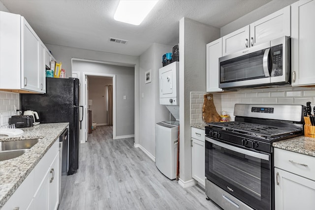 kitchen with light wood-type flooring, white cabinets, stainless steel appliances, and stacked washing maching and dryer