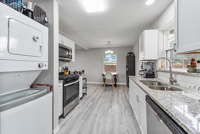 kitchen featuring appliances with stainless steel finishes, stacked washer and dryer, white cabinetry, and sink