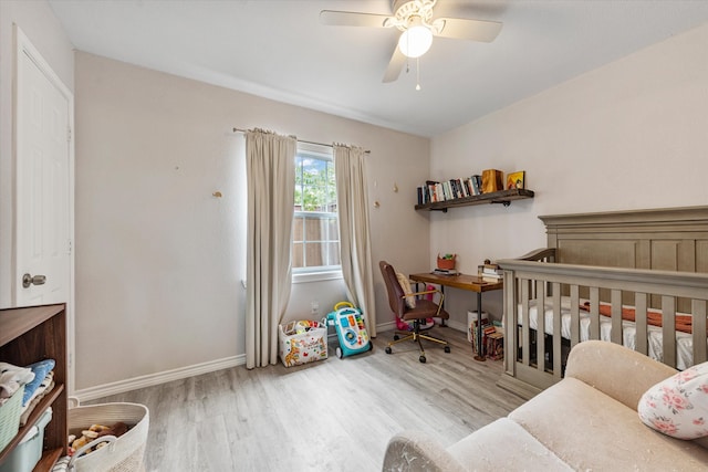 bedroom with a nursery area, ceiling fan, and light hardwood / wood-style floors