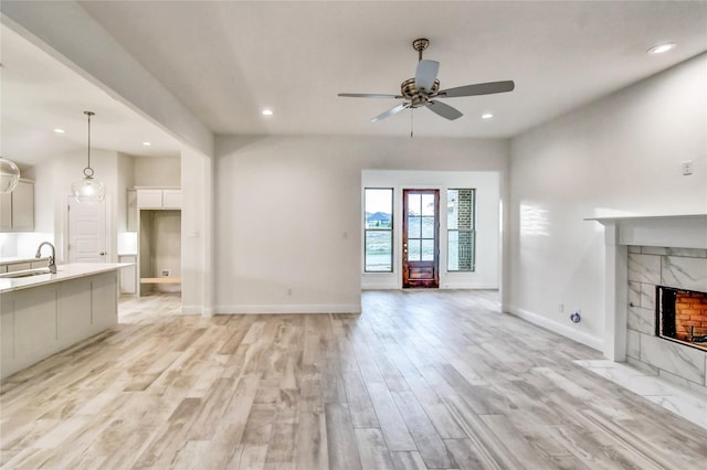 unfurnished living room featuring ceiling fan, a high end fireplace, sink, and light hardwood / wood-style floors