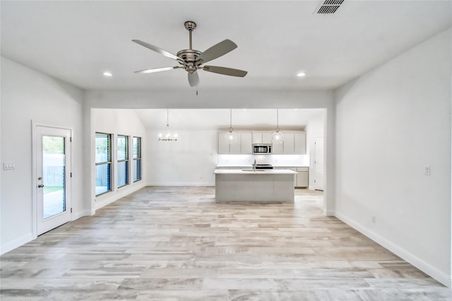 kitchen with a center island with sink, light hardwood / wood-style flooring, ceiling fan with notable chandelier, and hanging light fixtures