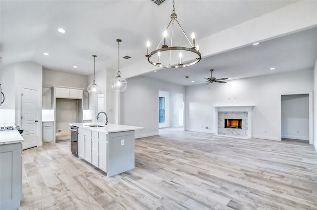 kitchen with hanging light fixtures, ceiling fan with notable chandelier, sink, an island with sink, and a premium fireplace