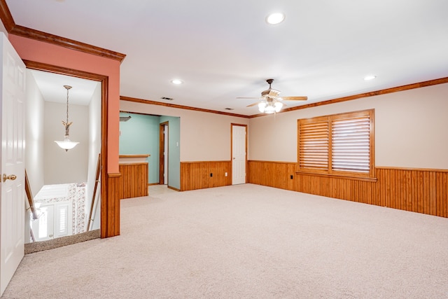 empty room with crown molding, wooden walls, ceiling fan, and carpet floors