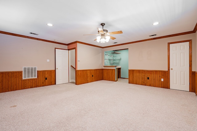 empty room featuring wood walls, ceiling fan, crown molding, and carpet floors