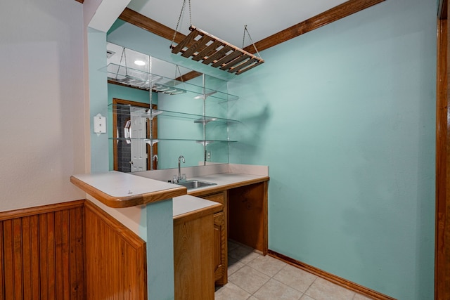 kitchen with wooden walls, crown molding, light tile patterned floors, kitchen peninsula, and sink