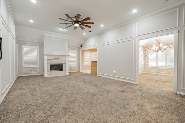 unfurnished living room featuring a tiled fireplace, vaulted ceiling, ceiling fan with notable chandelier, light carpet, and ornamental molding