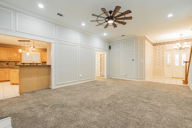 unfurnished living room featuring ceiling fan with notable chandelier, ornamental molding, and light colored carpet