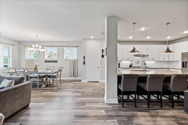 kitchen featuring white cabinets, a kitchen breakfast bar, wood finished floors, decorative light fixtures, and light stone countertops