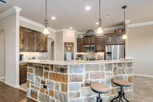 kitchen with dark brown cabinets, stainless steel appliances, a large island with sink, and a kitchen bar