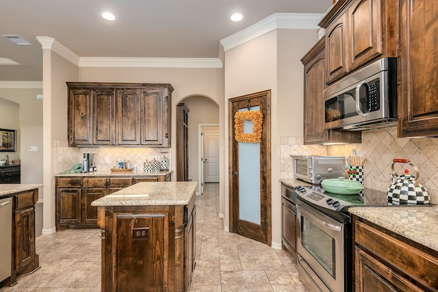 kitchen with ornamental molding, appliances with stainless steel finishes, light stone counters, and a center island