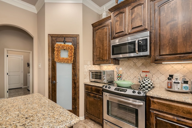 kitchen featuring dark brown cabinets, light stone counters, crown molding, and stainless steel appliances