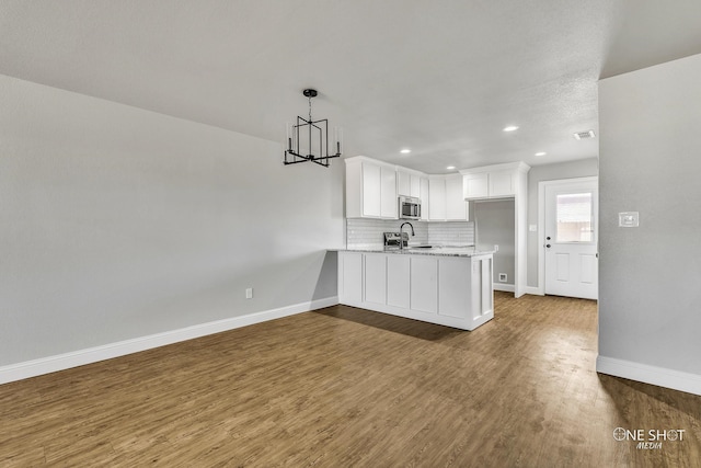 kitchen with kitchen peninsula, white cabinetry, decorative light fixtures, dark wood-type flooring, and a notable chandelier