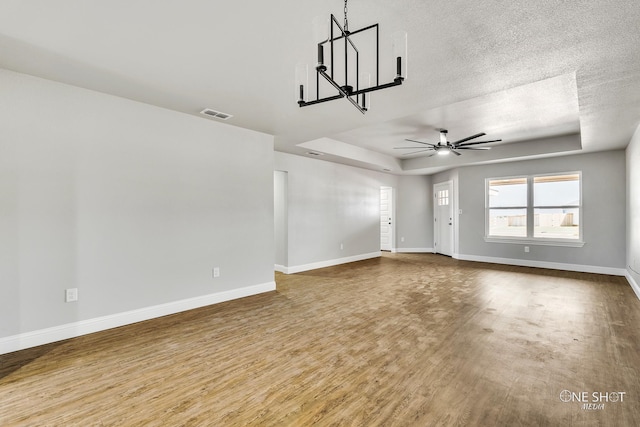 unfurnished living room featuring a textured ceiling, wood-type flooring, a tray ceiling, and ceiling fan with notable chandelier